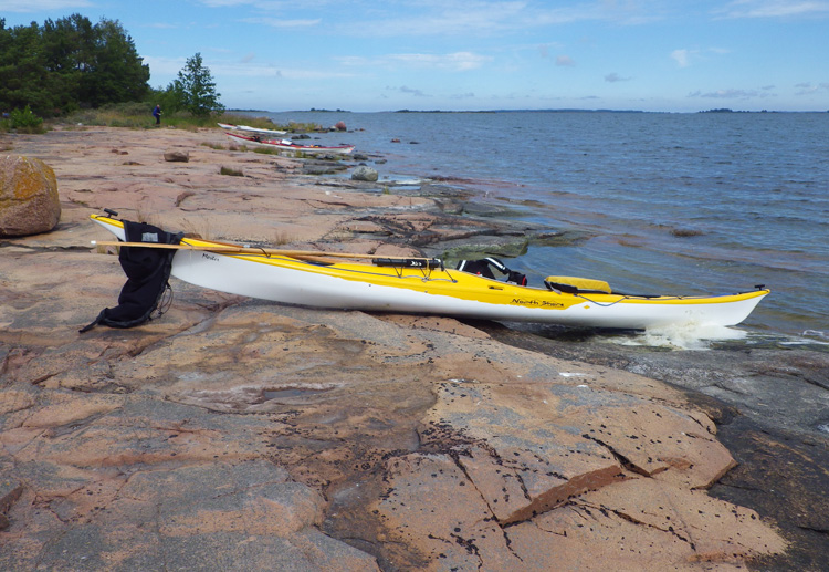 Bild. Kajaker uppdragna på den röda klippstranden.