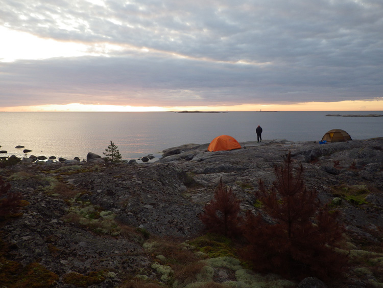 Bild. Strax efter soluppgången. Utsikten från skogen mot tälten och havet.