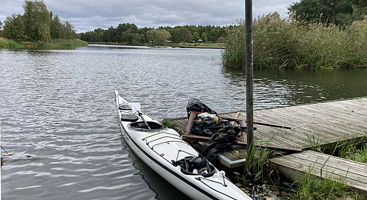 Bild. En kajak vid bryggan och några påsar skräp.