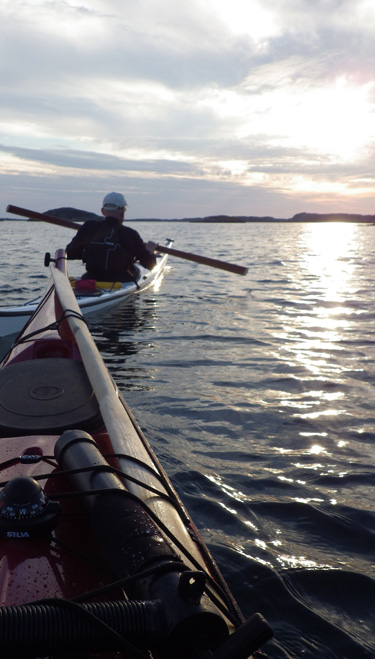 Bild. Första paddlingen med nya kajaken. Fören på min Nordkapp, Jan i hans kajak mot solnedgången.